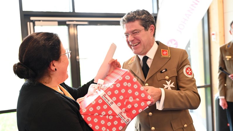 Auf dem Bild sind zwei Personen zu sehen. Eine Person erhält ein Geschnek. 