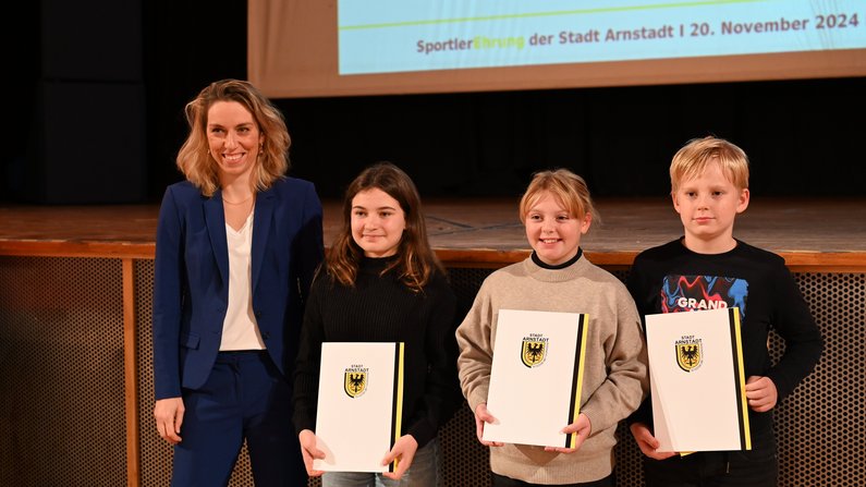 Auf dem Foto sind 3 Kinder und eine Frau zu sehen. Alle lächeln. Die Kinder halten eine Urkunde in den Händen. 