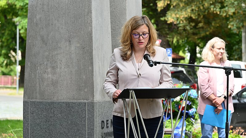 Auf dem Foto ist eine Frau zu sehen, sie hält eine Rede und spricht in ein Mikrofon. 