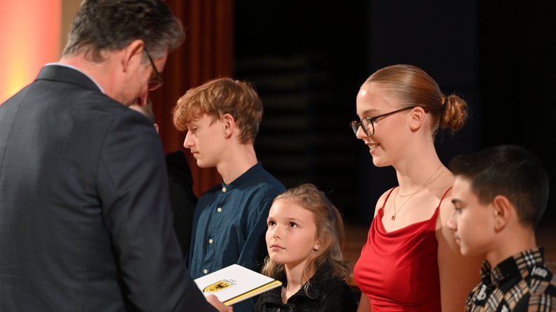 Auf dem Foto sind 5 Personen zu sehen. Ein Mann überreicht einem Kind eine Urkunde. 