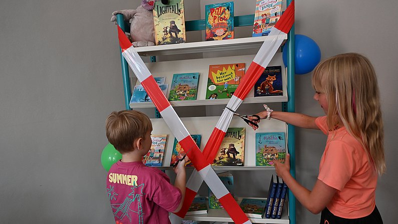 Auf dem Foto sind Kinder zu sehen, die ein rotes Band durchschneiden. 