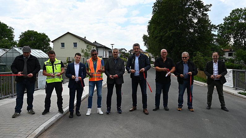Auf dem Foto sind 9 Männer zu sehen, die ein rotes Band durchschneiden. 